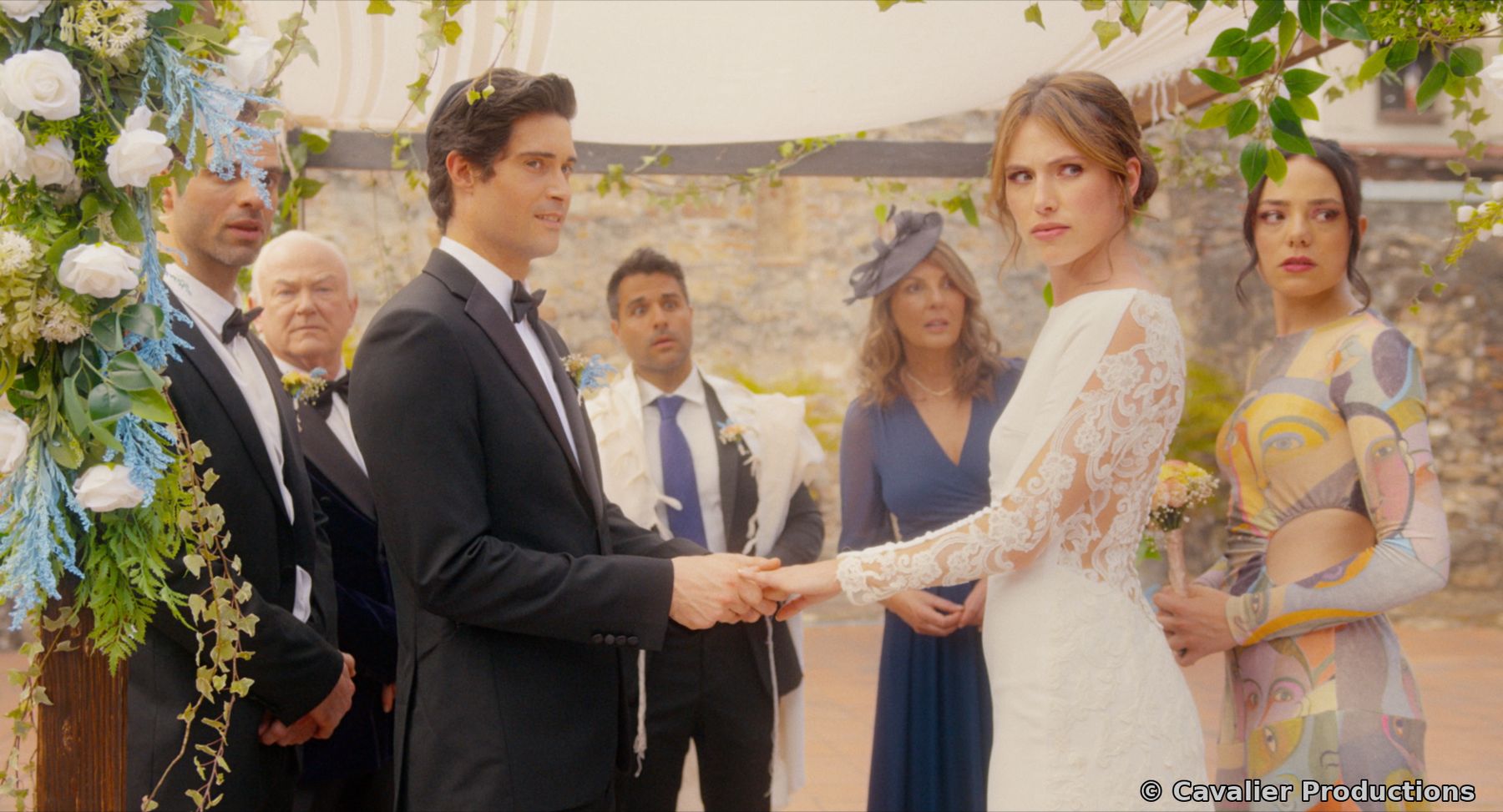 Dan and Liz holding hands under the chuppah, surrounded by wedding guests